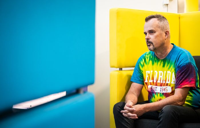 Kuvassa oikealla mies värikkäässä paidassa istumassa mietiskelevän näköisenä.