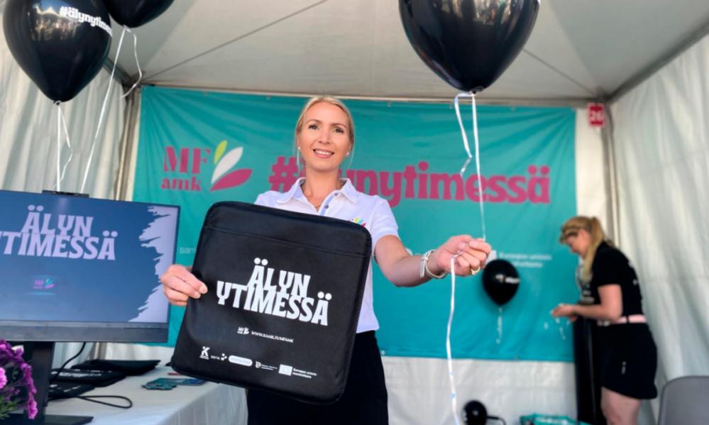 Kuvassa vaaleahiuksinen nainen pitää kädessään istuinalustaa ja ilmapalloa.