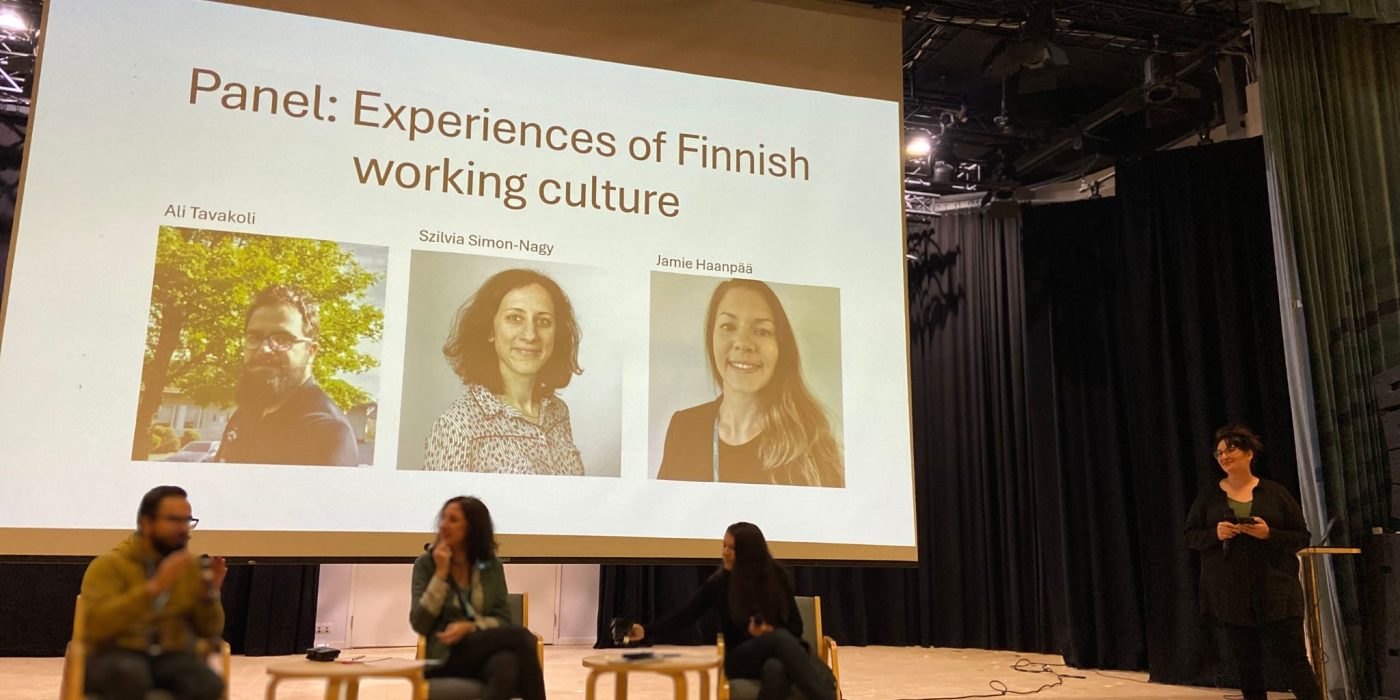 Kolme henkilöä lavalla istumassa tuoleille keskustelemassa.