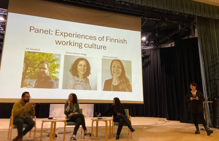 Kolme henkilöä lavalla istumassa tuoleille keskustelemassa.