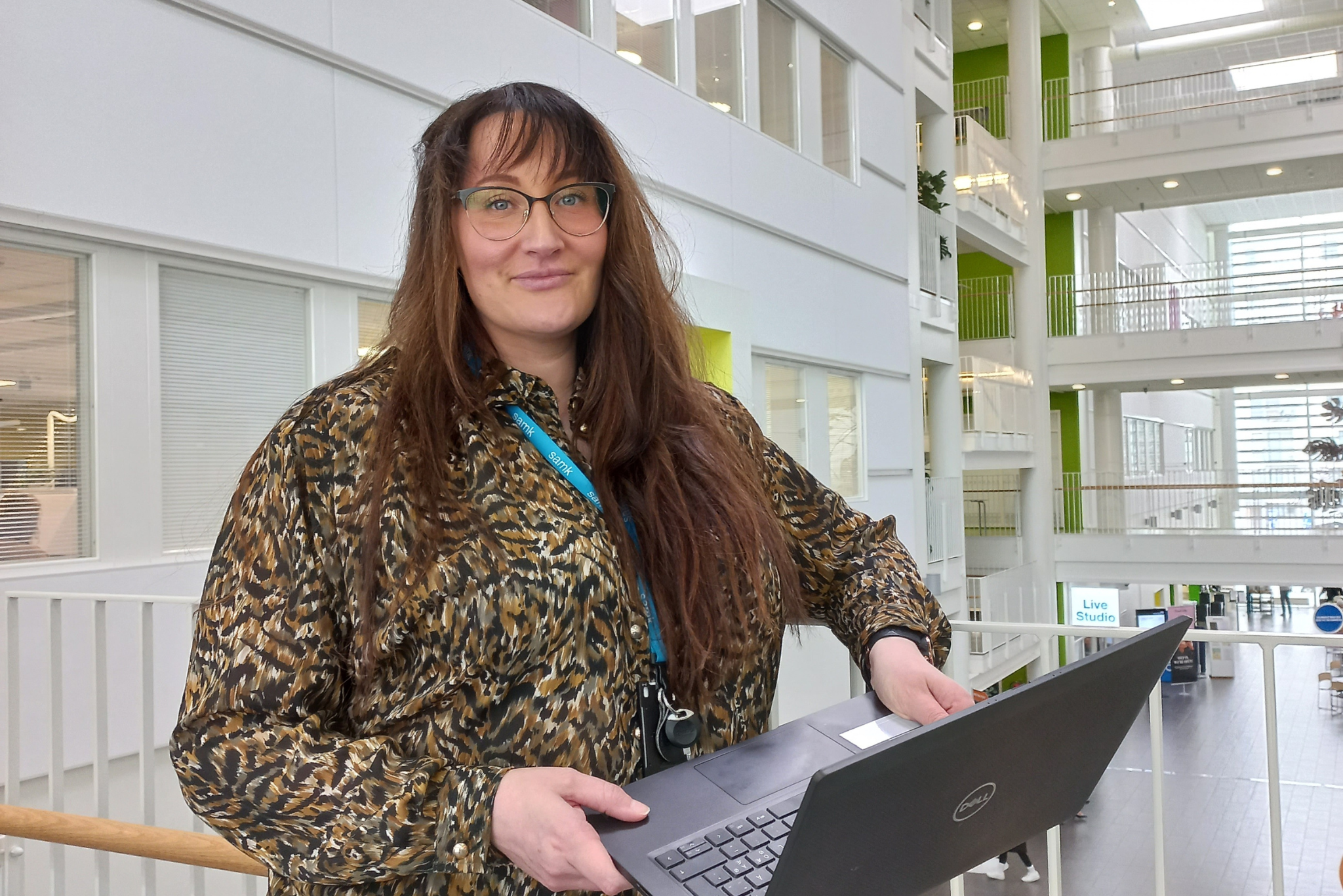 Kuvassa Minttu Porri, ruskeahiuksinen naine hymyilemässä pitäen tietokonetta käsissään.