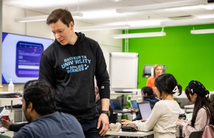 Henkilö seisomassa istuvien henkilöiden keskellä ja kädellä ohjeistamassa.