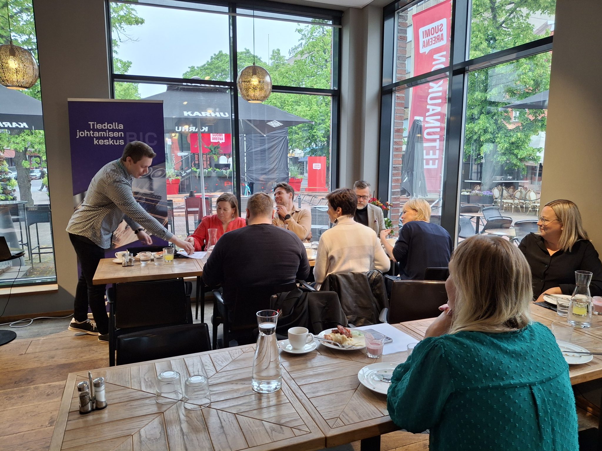 yleiskuvaa brunssitilaisuudesta. Ihmisiä istumassa pöytien ääressä ja nauttimassa brunssin antimista.