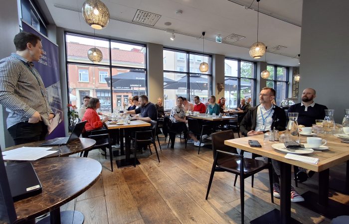 yleiskuvaa brunssitilaisuudesta. Ihmisiä istumassa pöytien ääressä ja nauttimassa brunssin antimista.