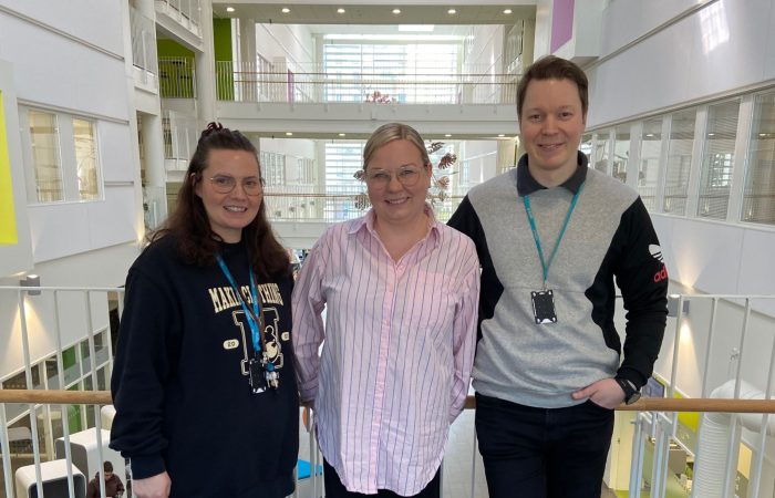 Lotta-Emilia, Paula, and Ollipekka are posing in the SAMK lobby.