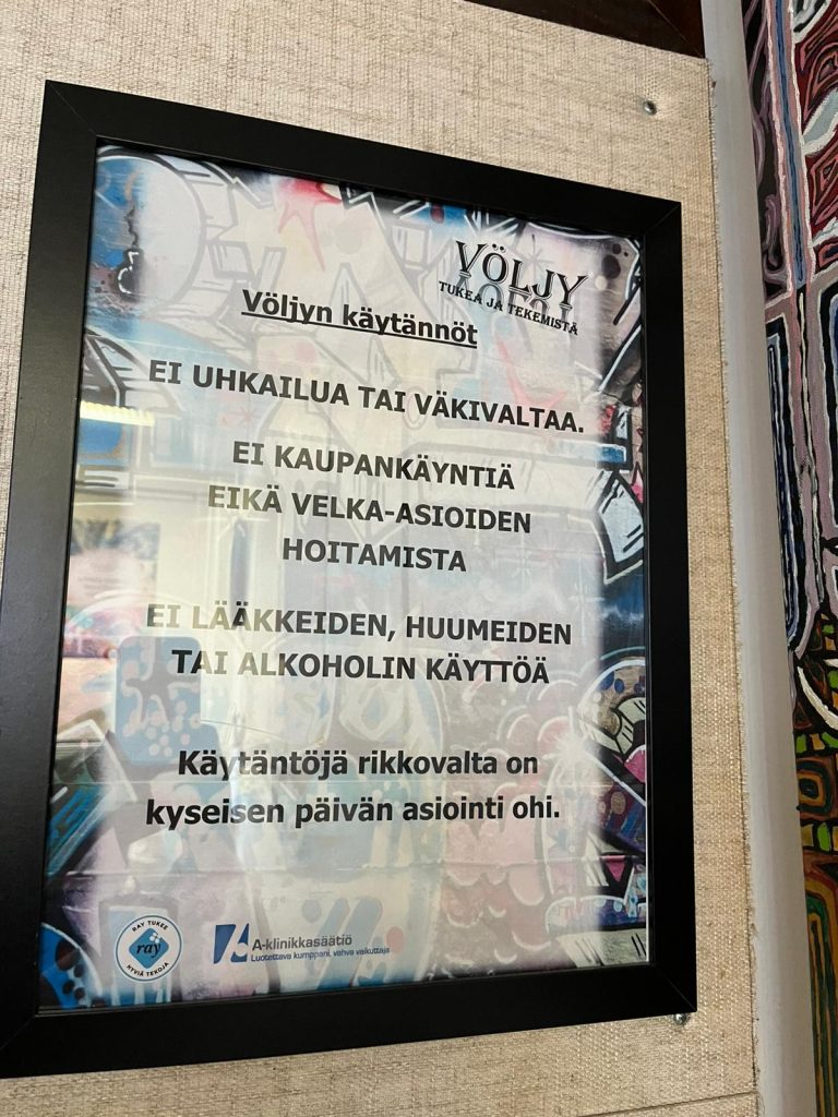 Seinälle kiinnitetty mustakehyksinen opaste, jossa listataan Völjy-toiminnan käytännöt graffititaustaa vasten.