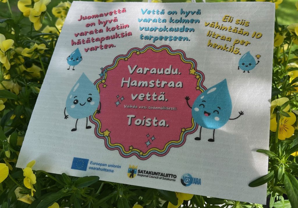 Vesivara-tiskirätti kukkien keskellä muistuttaa kotitalouksien vesivarautumisesta häiriötilanteissa.