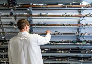 Laboratoriotilanne, jossa henkilö valkotakissa tarkastelee seinälle asennettuja putkirivejä ja venttiilejä.
