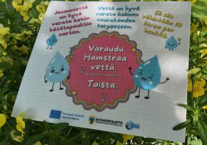 Vesivara-tiskirätti kukkien keskellä muistuttaa kotitalouksien vesivarautumisesta häiriötilanteissa.