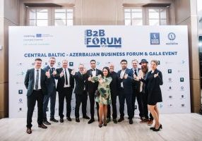 Ryhmä ihmisiä poseeraa yhdessä B2B Forum -tapahtuman taustaseinän edessä.