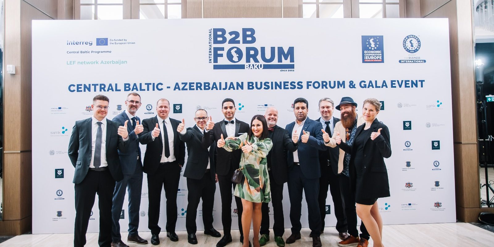 Ryhmä ihmisiä poseeraa yhdessä B2B Forum -tapahtuman taustaseinän edessä.