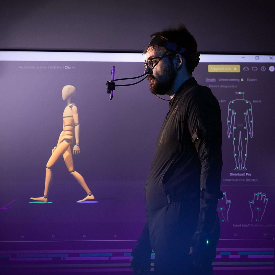 Lilasävyisessä kuvassa miehellä on päällään motioncapture-puku ja päässään kamera.