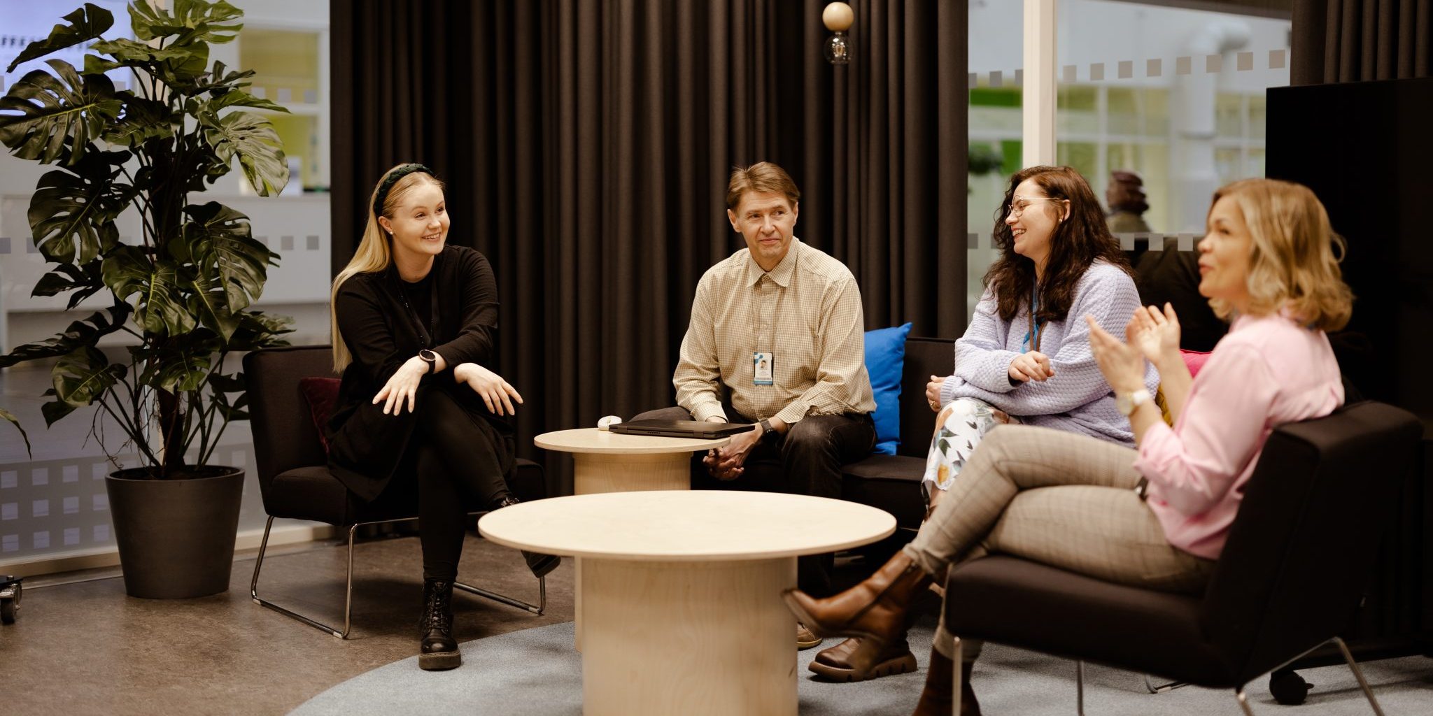 Four smiling people sitting on a sofa and armchairs.