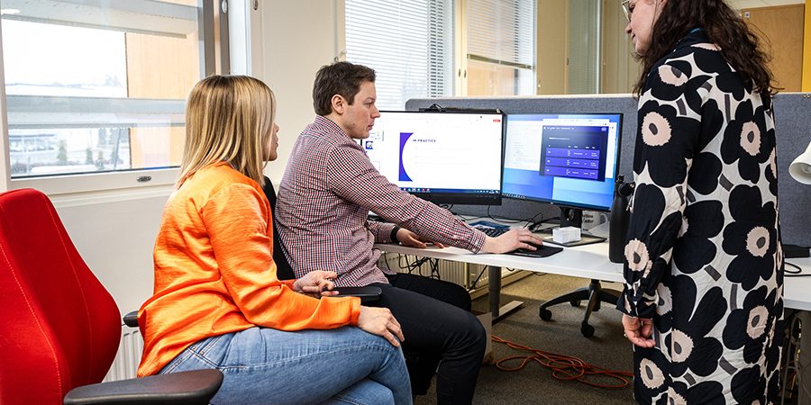 Kolme ihmistä katselee yhdessä tietokoneelta dataa.